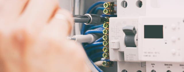 Elektryk przykręcający śrubokrętem przewody do wyłącznika różnicowoprądowego w rozdzielnicy elektrycznej.