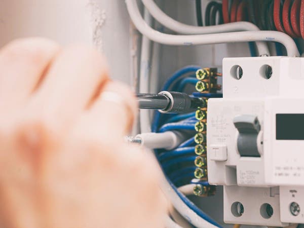 Elektryk przykręcający śrubokrętem przewody do wyłącznika różnicowoprądowego w rozdzielnicy elektrycznej.