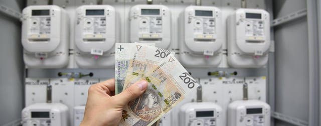 Dłoń trzymająca 500 zł na tle skrzynki z licznikami elektrycznymi.