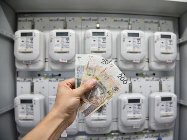 Dłoń trzymająca 500 zł na tle skrzynki z licznikami elektrycznymi.