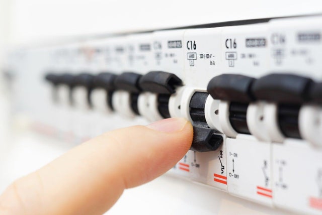 Zbliżenie na palec przełączający wyłącznik nadprądowy C16 w rozdzielnicy elektrycznej z rzędem bezpieczników.