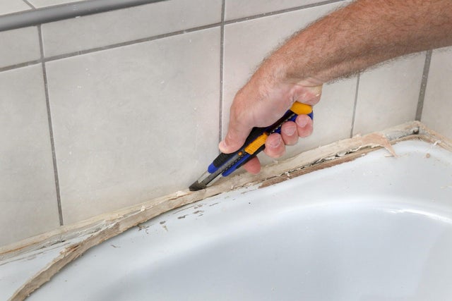Usuwanie starego silikonu przy wannie za pomocą nożyka technicznego.