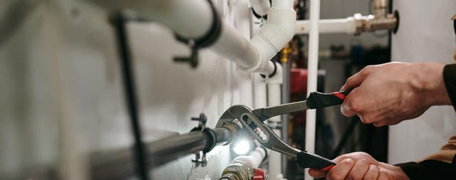 Dokręcanie połączenia rur instalacji hydraulicznej kluczem w pomieszczeniu technicznym.
