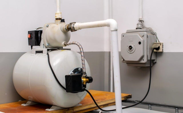 Domowy hydrofor z pompą i instalacją wodną zamontowany przy ścianie pomieszczenia technicznego.