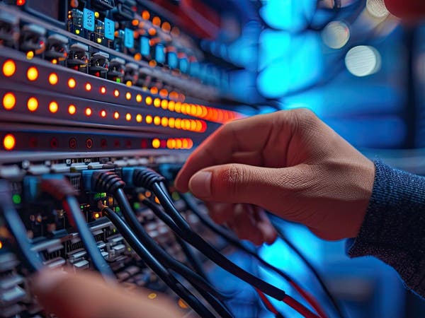 Technik podłączający kable sieciowe do rozświetlonego panelu serwerowego z pomarańczowymi diodami LED w centrum danych.