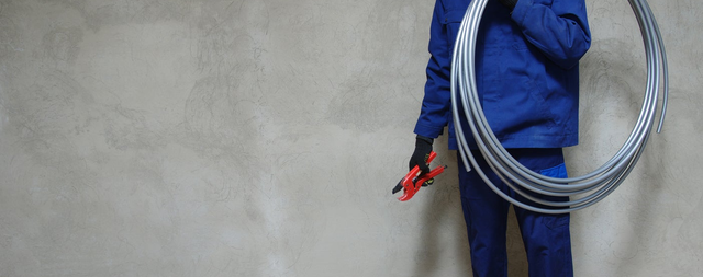 Instalator trzyma zwój elastycznych rur PEX i narzędzie do cięcia.