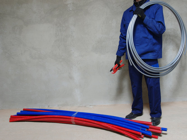 Instalator trzyma zwój elastycznych rur PEX i narzędzie do cięcia.
