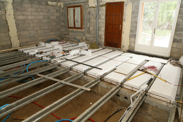 Montaż systemu ogrzewania podłogowego z rurami i izolacją styropianową podczas budowy domu.