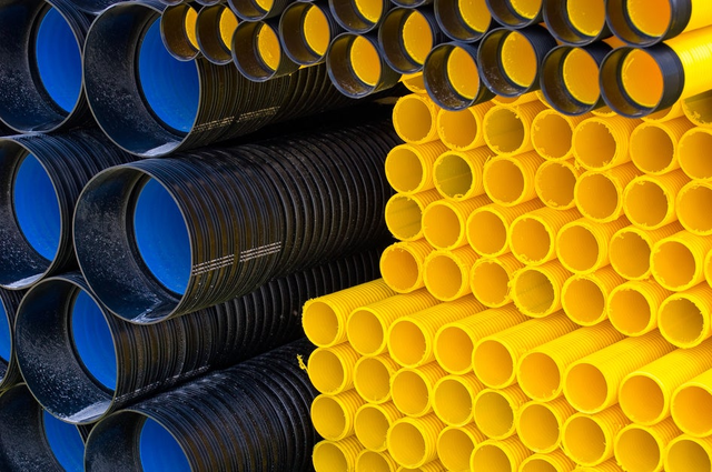 Składowane rury karbowane HDPE w kolorze czarnym i żółtym do instalacji kanalizacyjnych i elektrycznych.