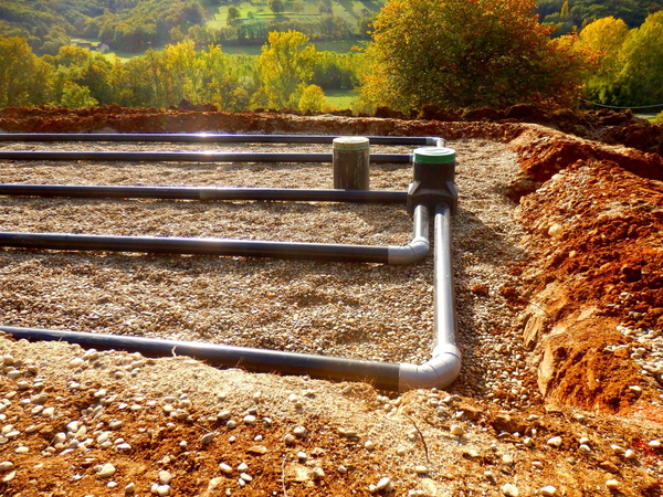Instalacja podziemnego systemu drenażowego z rur PVC na żwirowym podłożu przy budowie domu.