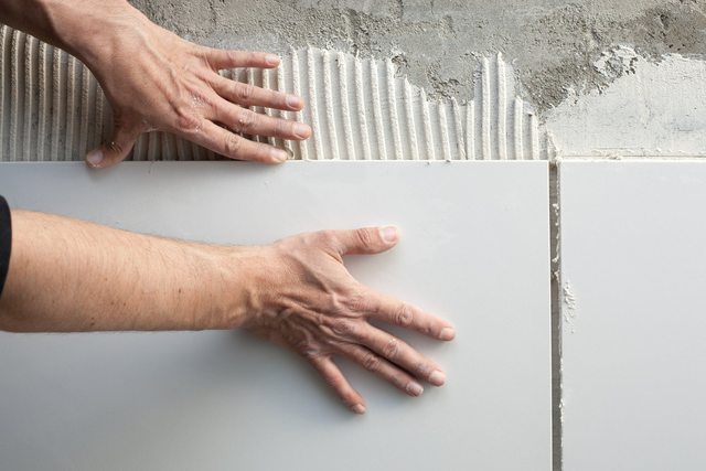Układanie dużych białych płytek ceramicznych na zaprawie klejowej podczas remontu ściany.