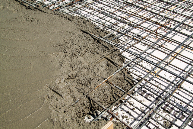 Wylewanie betonu na siatkę zbrojeniową podczas wykonywania żelbetowej płyty fundamentowej na placu budowy.