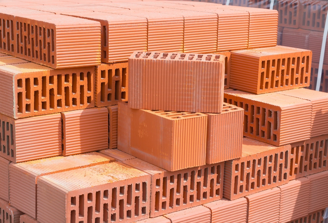 Paleta pomarańczowych pustaków ceramicznych ułożonych na placu budowy jako materiał do wznoszenia ścian nośnych i działowych.