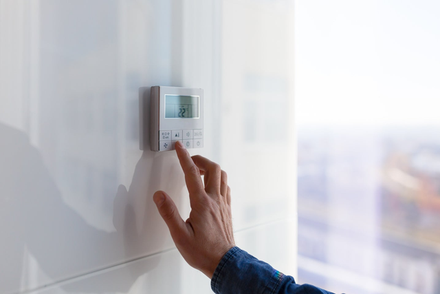 Dłoń naciskająca przycisk elektronicznego regulatora klimatyzacji z wyświetlaczem pokazującym temperaturę 22°C.