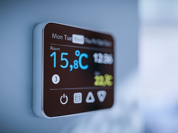 Inteligentny termostat ścienny z kolorowym wyświetlaczem pokazującym aktualną temperaturę 15,8°C i zadaną 22°C z harmonogramem tygodniowym.