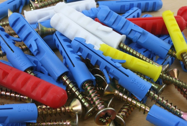 Kolorowe kołki rozporowe plastikowe w rozmiarze 8x40 w kolorach niebieskim, białym, żółtym i czerwonym z wkrętami rozsypane na drewnianej powierzchni.