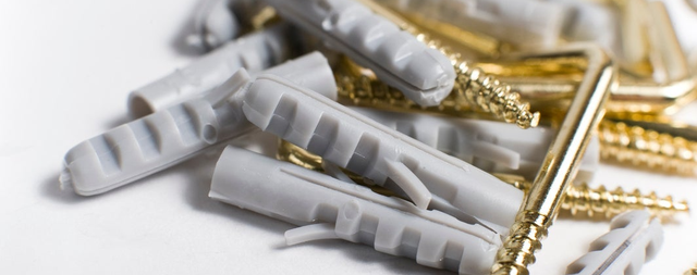 Szare plastikowe kołki rozporowe z złotymi wkrętami samogwintującymi rozsypane na białym tle.