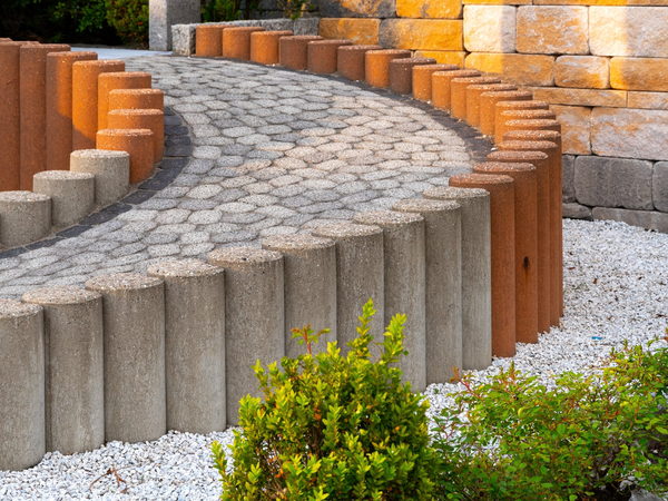 Wykończenie krętej alejki kostką brukową obramowaną palisadami betonowymi i ceglanymi.