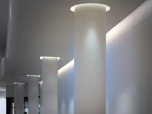 Nowoczesne białe kolumny architektoniczne z podświetleniem LED w suficie eleganckiego lobby budynku biurowego lub hotelowego.