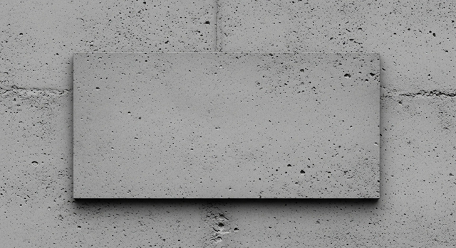 Dekoracyjna płyta z betonu architektonicznego z charakterystyczną porowatą fakturą na tle szarej ściany betonowej do wykończenia wnętrz.