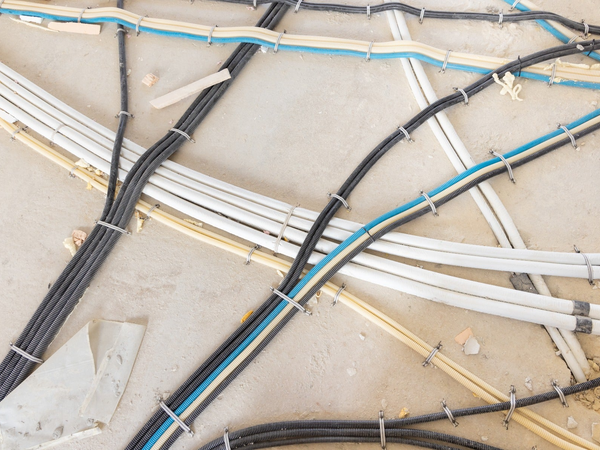 Sieć rur instalacyjnych i przewodów elektrycznych w karbowanych osłonach różnych kolorów przypiętych do betonowej posadzki budynku w stanie surowym.