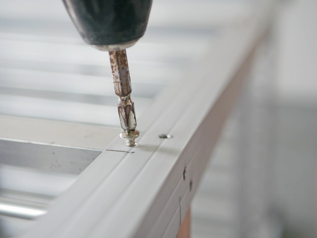 Wkręcanie śruby w profil aluminiowy żaluzji za pomocą wkrętarki.