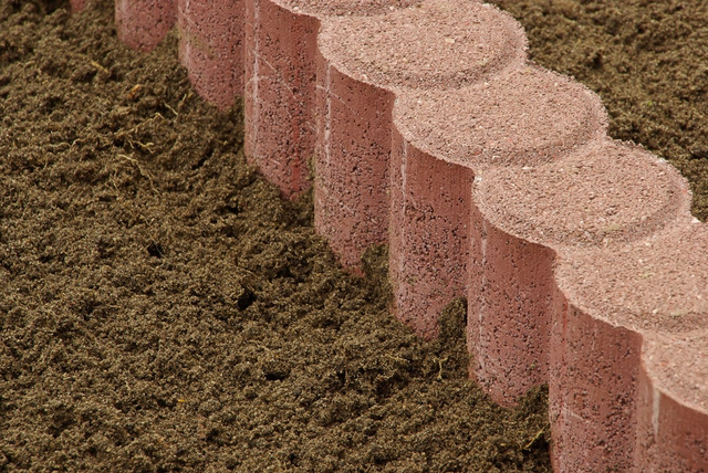 Układanie obrzeży ogrodowych z czerwonej kostki palisadowej na podsypce piaszczystej.