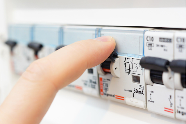 Dłoń naciskająca wyłącznik różnicowoprądowy 30mA C10 w rozdzielnicy elektrycznej podczas obsługi instalacji elektrycznej.