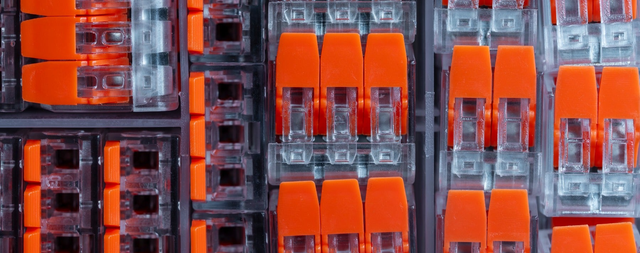 Zestaw pomarańczowo-przezroczystych złączek sprężynowych do przewodów elektrycznych ułożonych w plastikowym pojemniku sortowniczym.