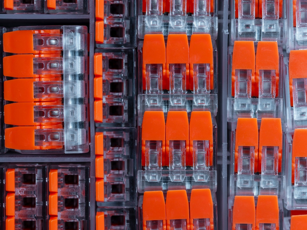 Zestaw pomarańczowo-przezroczystych złączek sprężynowych do przewodów elektrycznych ułożonych w plastikowym pojemniku sortowniczym.