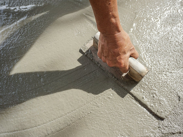 Dłoń murarza wyrównuje mokry beton pacą na posadzce podczas prac wykończeniowych.