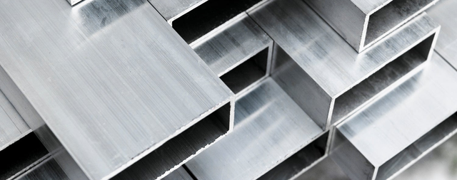 Zbliżenie na prostokątne profile aluminiowe ułożone w stos.
