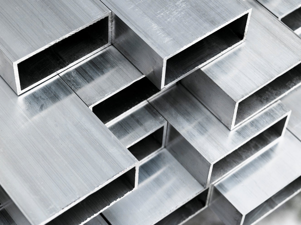 Zbliżenie na prostokątne profile aluminiowe ułożone w stos.
