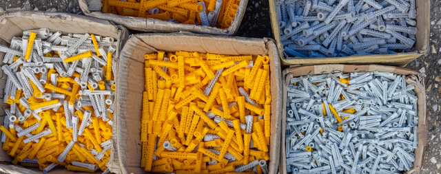 Kartonowe pudełka wypełnione po brzeg plastikowymi kołkami rozporowymi w kolorze żółtym i szarym.