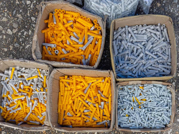 Kartonowe pudełka wypełnione po brzeg plastikowymi kołkami rozporowymi w kolorze żółtym i szarym.