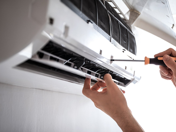 Serwisant naprawia otwarty klimatyzator ścienny śrubokrętem w trakcie przeglądu urządzenia.