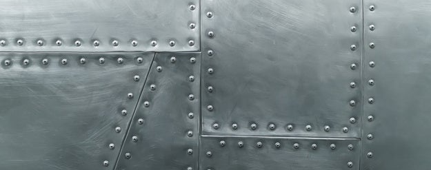 Aluminiowa powierzchnia z rzędami nitów łączących panele w metalowej konstrukcji przemysłowej.