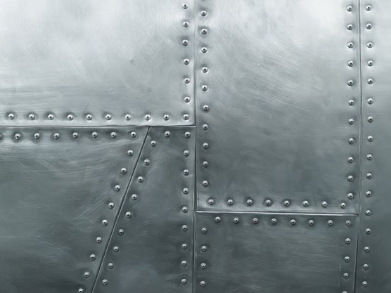 Aluminiowa powierzchnia z rzędami nitów łączących panele w metalowej konstrukcji przemysłowej.