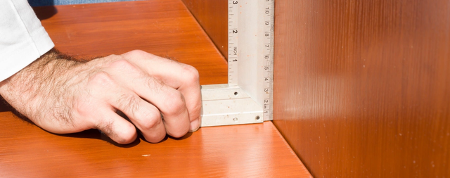 Dłoń przykłada kątownik do narożnika drewnianego mebla podczas montażu za pomocą wkrętarki.