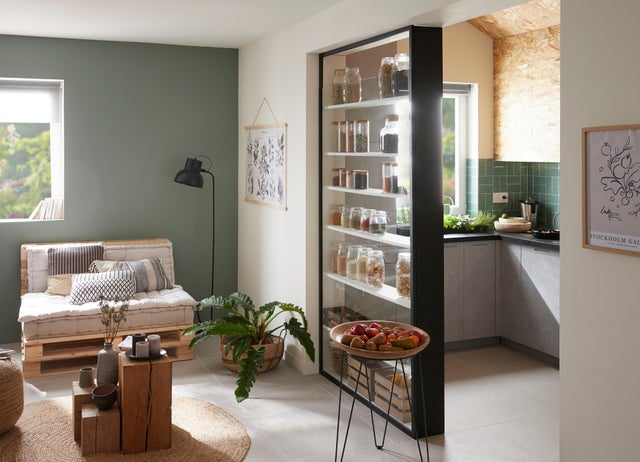 Photo Leroy Merlin d'un salon avec un mur vert et une cuisine semi-ouverte avec des étagères où ranger les bocaux entre le salon et la cuisine. 