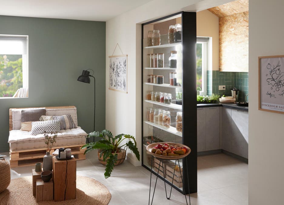 Photo Leroy Merlin d'un salon avec un mur vert et une cuisine semi-ouverte avec des étagères où ranger les bocaux entre le salon et la cuisine. 